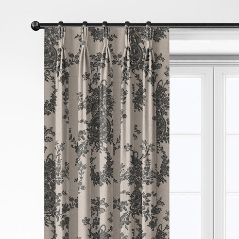 Close-up of Country Lane Ebony pleated drapery hanging from rings, with dark floral and medallion motifs on a beige background.