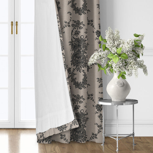 Country Lane Ebony patterned drapery panel turned back to reveal white lining beside a silver table with a vase of flowers.