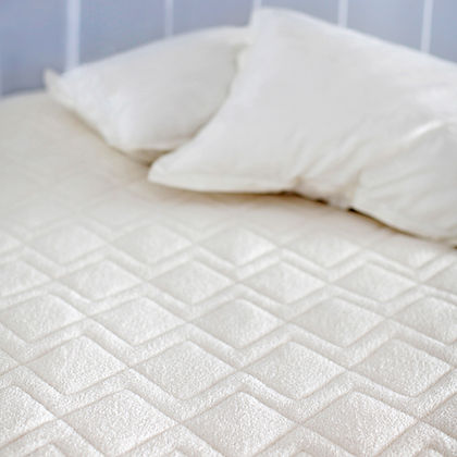 Close-up of St. Genève Dormeir® diamond-quilted wool mattress protector on a bed with pillows