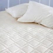 Close-up of St. Genève Dormeir® diamond-quilted wool mattress protector on a bed with pillows