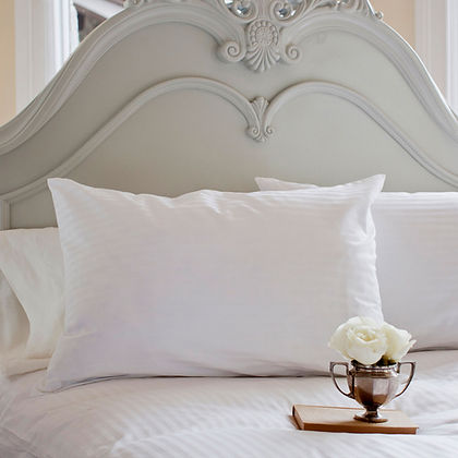 St. Genève Luxury Pillow Protector on a white pillow with ornate grey headboard and white rose accent
