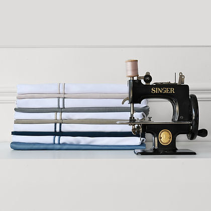 St. Genève Capri Double Satin Stitch sheets in multiple colours folded beside a vintage Singer sewing machine