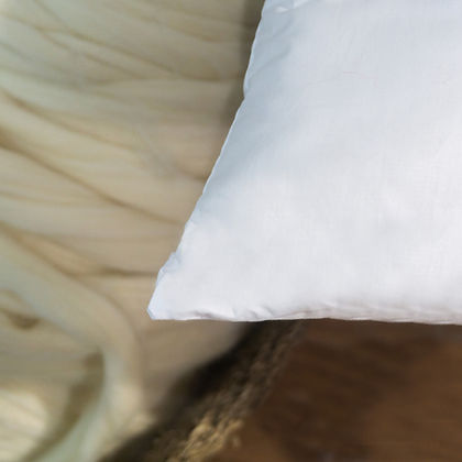 Close-up of St. Genève Piatra Merino wool pillow on a linen bed with natural wool texture in the background