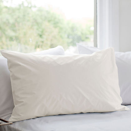 St. Genève Organic Pillow Protector in natural white cotton on a bed near a bright window