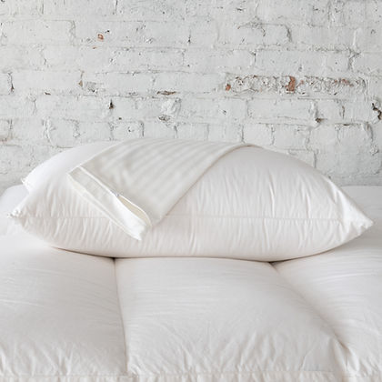 St. Genève Luxury Pillow Protectors stacked on a bed against a white brick wall
