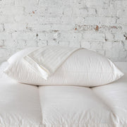 St. Genève Luxury Pillow Protectors stacked on a bed against a white brick wall