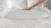 Hand resting on a St. Genève Piatra wool pillow placed on a white quilted bed