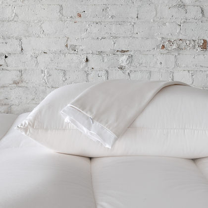 St. Genève Absolute Pillow Protector on a bed with white pillows against a white brick wall