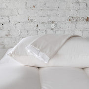 St. Genève Absolute Pillow Protector on a bed with white pillows against a white brick wall