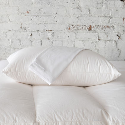 St. Genève Allergy Pillow Protectors stacked on a bed against a white brick wall