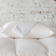 St. Genève Allergy Pillow Protectors stacked on a bed against a white brick wall