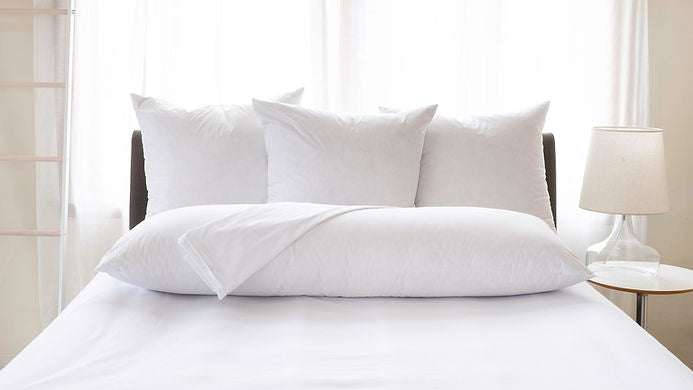 St. Genève luxury body pillow in white pillowcase resting at the foot of a neatly made bed with sheer curtains