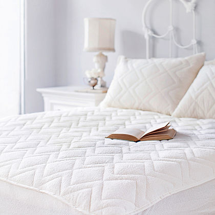St. Dormeir® quilted wool mattress protector on a bed with open book, bright white bedroom