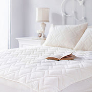 St. Dormeir® quilted wool mattress protector on a bed with open book, bright white bedroom