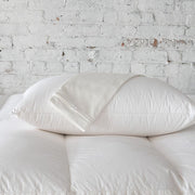 St. Genève Organic Pillow Protector covering fluffy white pillows against a white brick wall