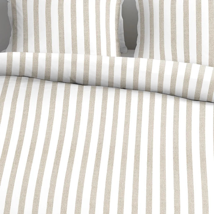 closer view: Close-up of Ally sand and white striped cotton duvet cover folded back beneath matching pillows