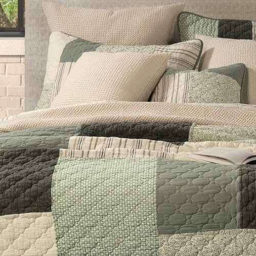 Broccolini green and cream patchwork quilt on a bed with coordinating pillow shams beneath a large window overlooking trees