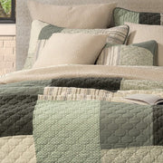 Broccolini green and cream patchwork quilt on a bed with coordinating pillow shams beneath a large window overlooking trees