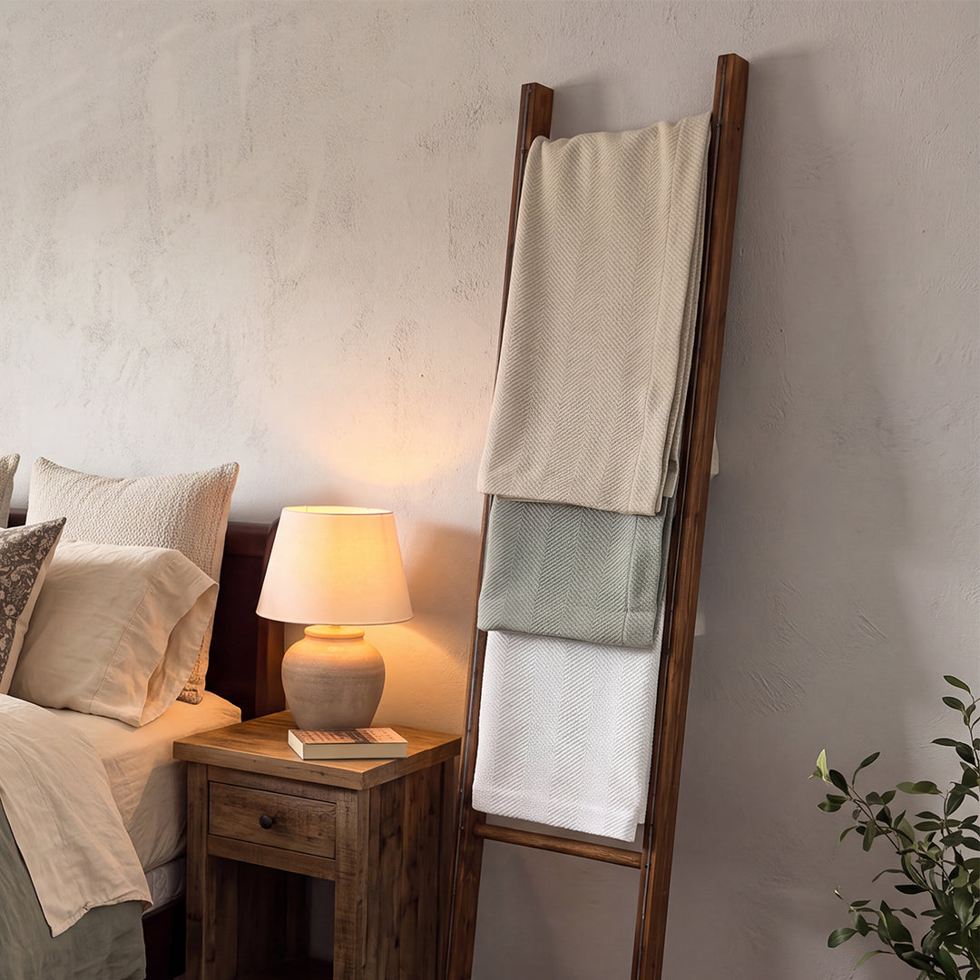 Cuddle Down Chevron cotton blankets draped on a wooden ladder in a cozy bedroom setting – available in white, sea glass, and pebble
