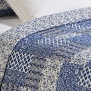 Donalda blue and ivory patchwork style quilt set on a bed