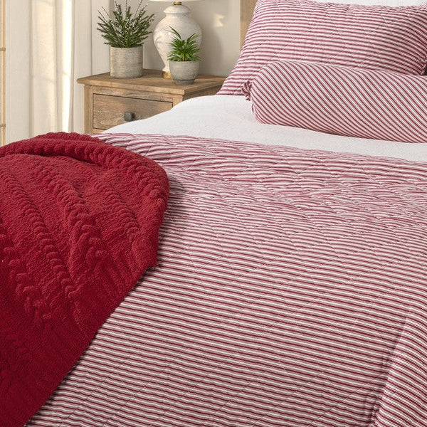 Close-up of the Holly red and white striped quilt showing its quilted texture beside a red throw and matching striped pillows.
