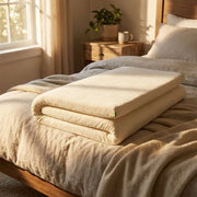 Natura Ultimate Latex Topper folded on a bed in a warm sunlit bedroom with organic cotton cover