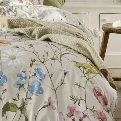 closer view: Close-up of Melodie floral duvet cover with pastel wildflowers and green stems, styled with a green throw