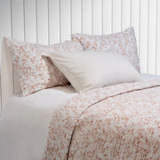 Marjolaine quilt set in white with warm terracotta foliage print, styled on a bed with matching pillow shams
