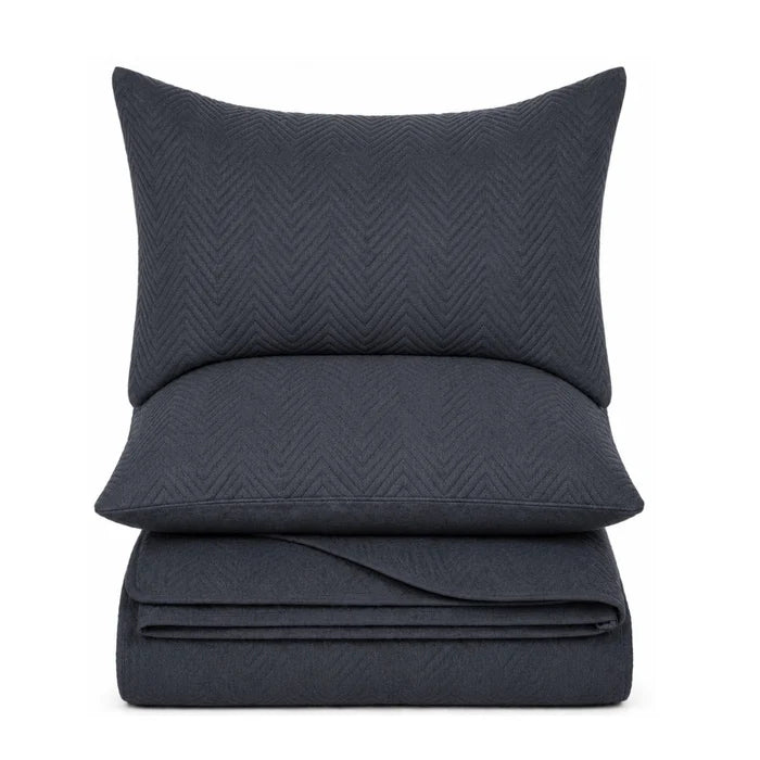 A dark navy blue bedding set featuring a pillowcase, a folded sheet or duvet cover, and a matching folded pillow, all with a subtle textured chevron pattern, shown against a plain white background.