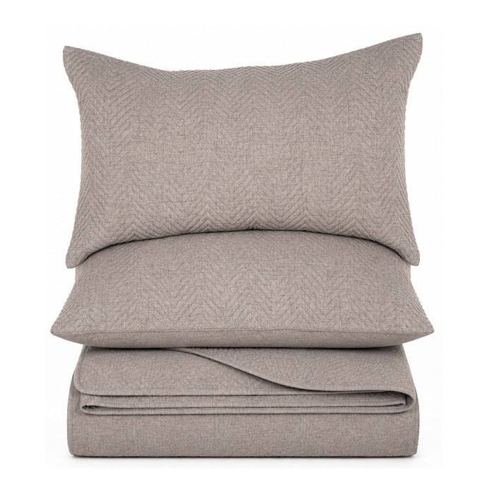 A stack of three light taupe-gray textured bedding pieces, including a pillowcase, a flat pillow, and a folded sheet, shown against a solid white background.