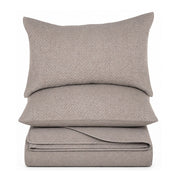 A stack of three light taupe-gray textured bedding pieces, including a pillowcase, a flat pillow, and a folded sheet, shown against a solid white background.