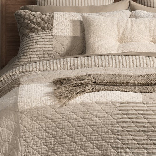 Close-up of Panorama patchwork quilt in natural, ivory and taupe with quilted stitching and a striped reverse folded back