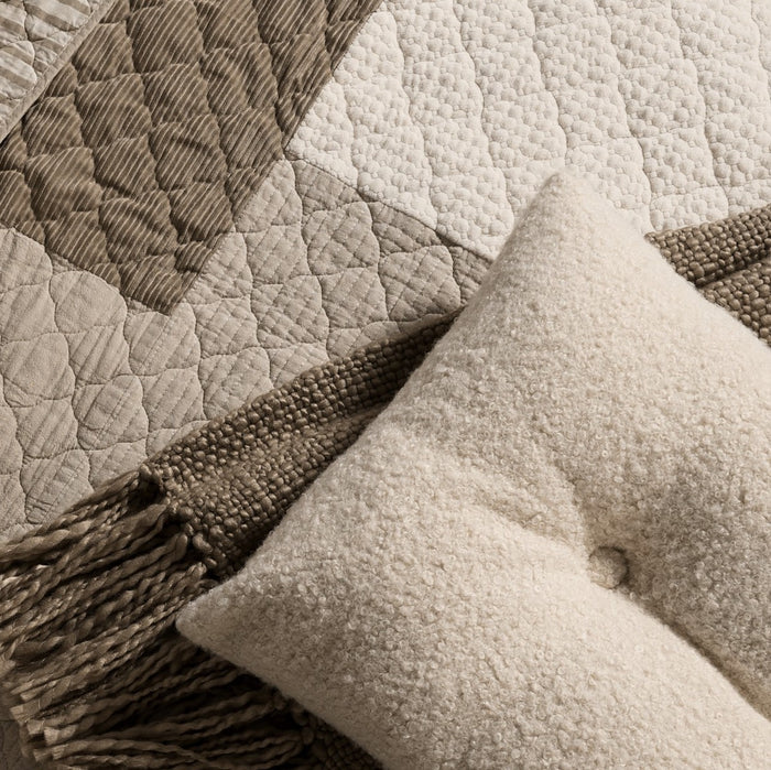 Close-up of Panorama quilt with ivory dotted and taupe striped patchwork beside a textured cushion and fringed throw.