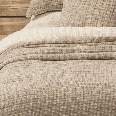 Close-up of the Spirit taupe cotton quilt showing its waffle texture and folded edge over cream bedding.