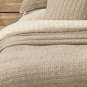 Close-up of the Spirit taupe cotton quilt showing its waffle texture and folded edge over cream bedding.